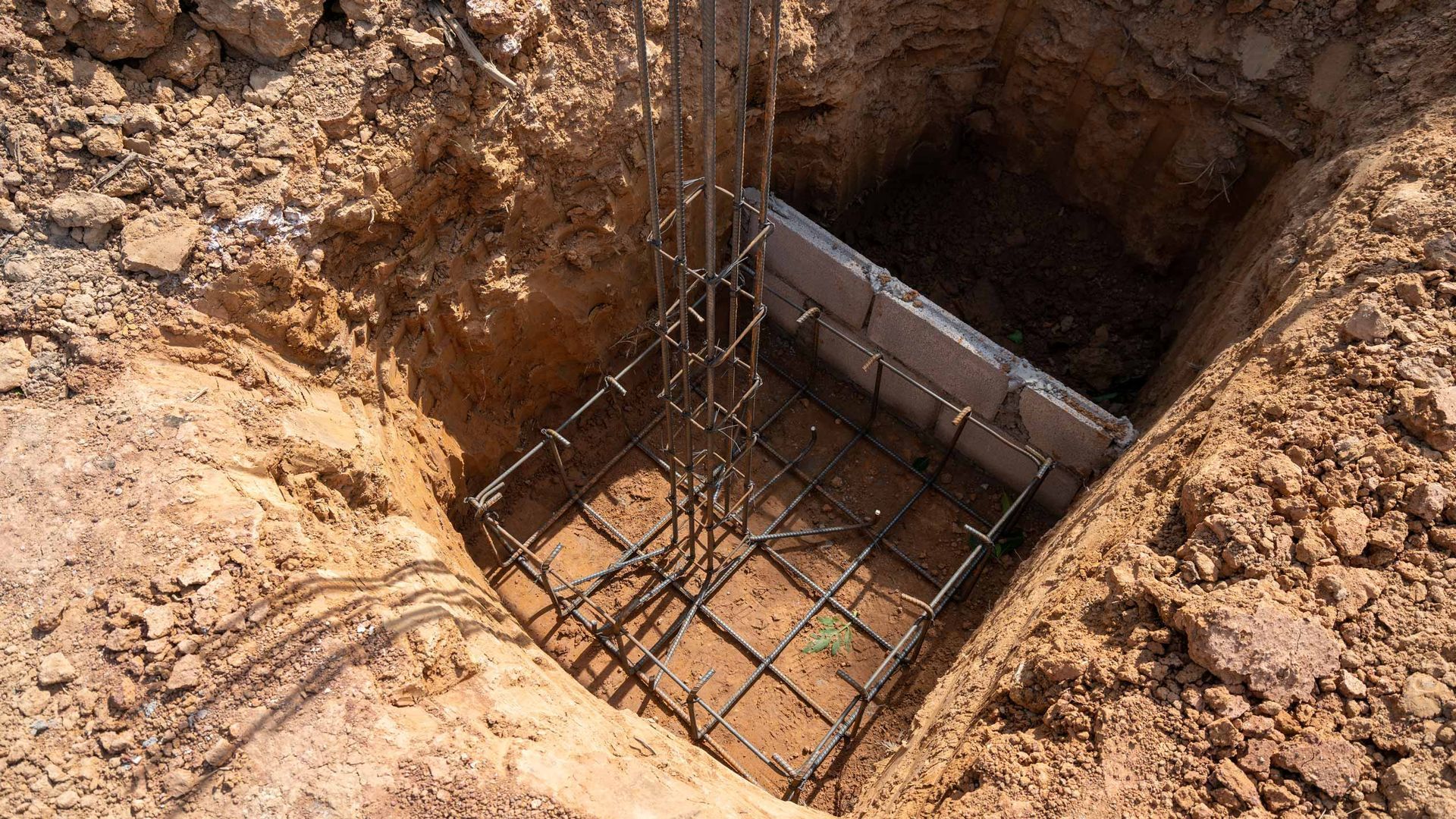 Rebar and concrete footing in a dug foundation pit surrounded by dirt soil