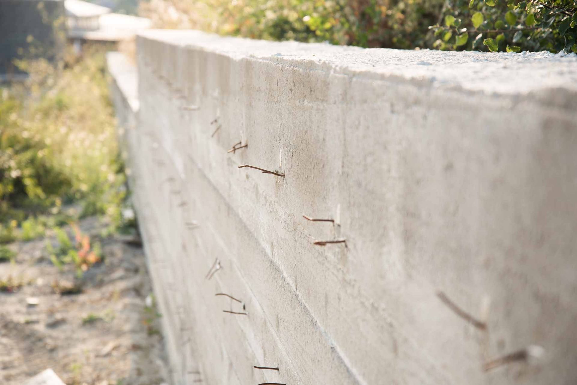Concrete wall with small metal protrusions beside a blurred grassy path