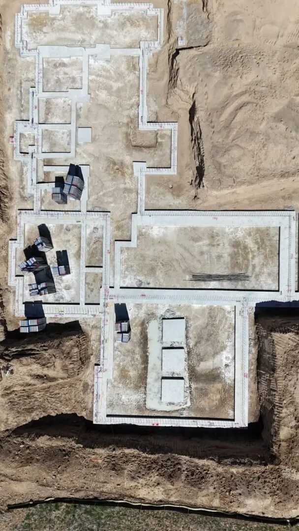 Aerial view of a building foundation layout with white marked walls and small square footings on brown soil.