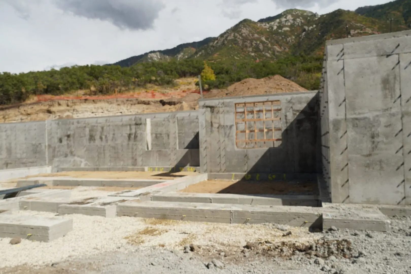 Concrete foundation wall and stairwell under construction beside a rocky hillside.