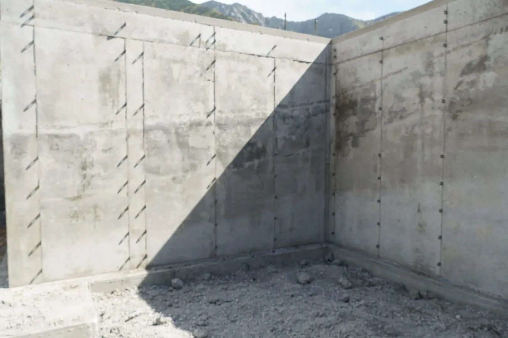 Bare concrete walls forming a corner with a diagonal shadow and dusty floor in an unfinished structure