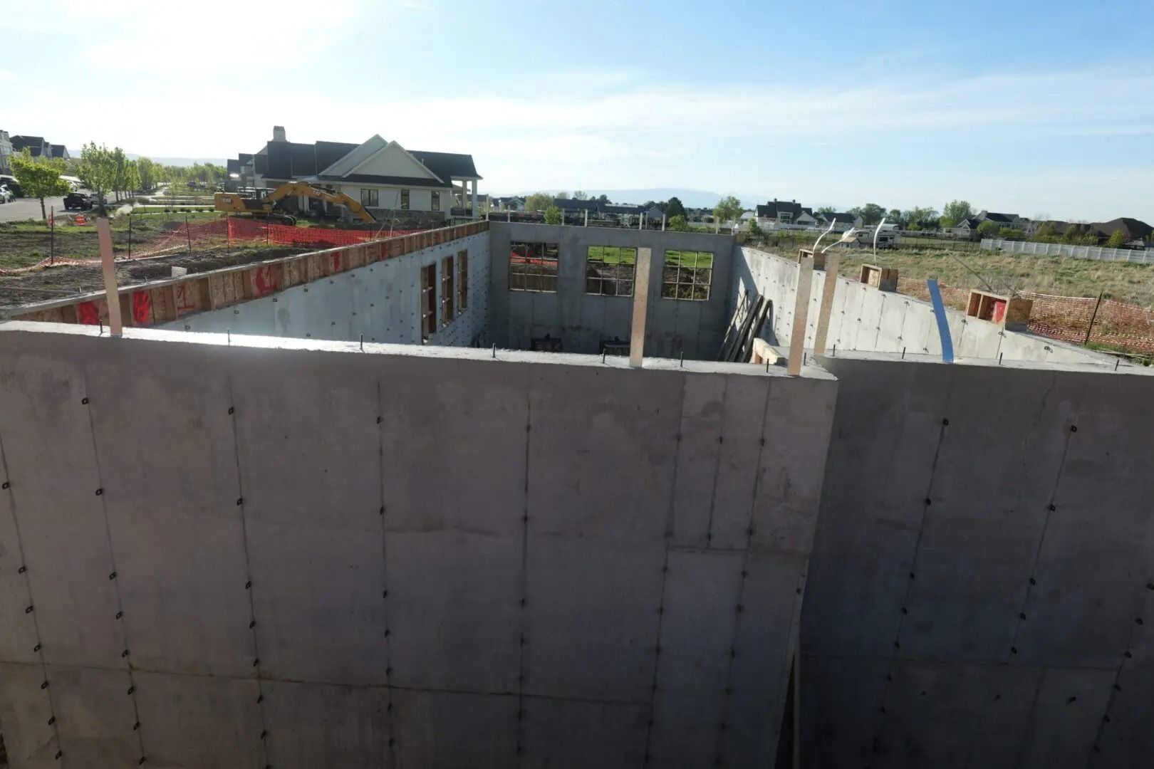 Concrete building foundation under construction with open excavation and a house in the distance.