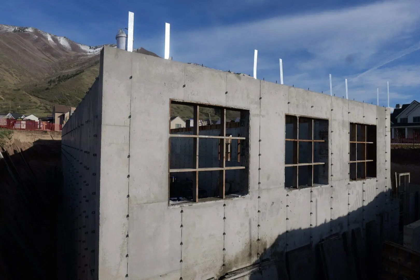 Concrete building with large windows on a sunny mountainside, with snow-capped peaks in the background