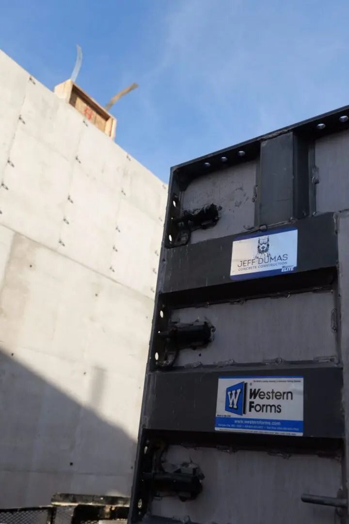 Black industrial wall with two white signs, one reading “Northern Formas,” beside a concrete building.