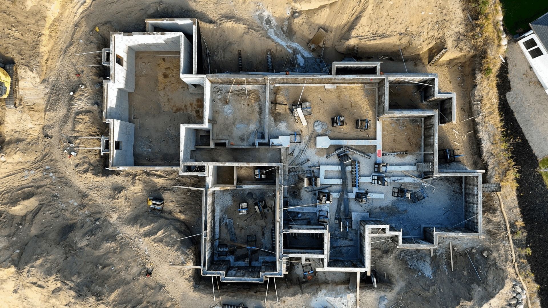 Aerial view of a partially excavated house foundation with interior rooms exposed in a dirt lot