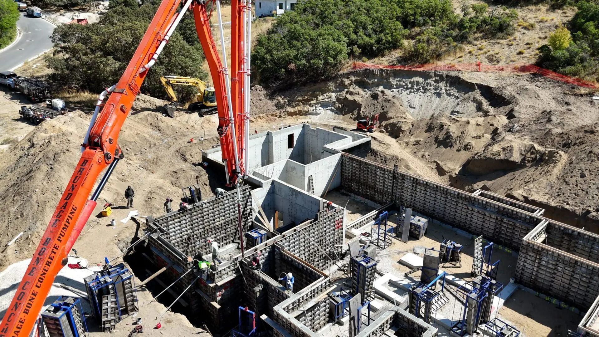 Orange excavator lifting concrete forms at a construction site with rebar and a deep trench