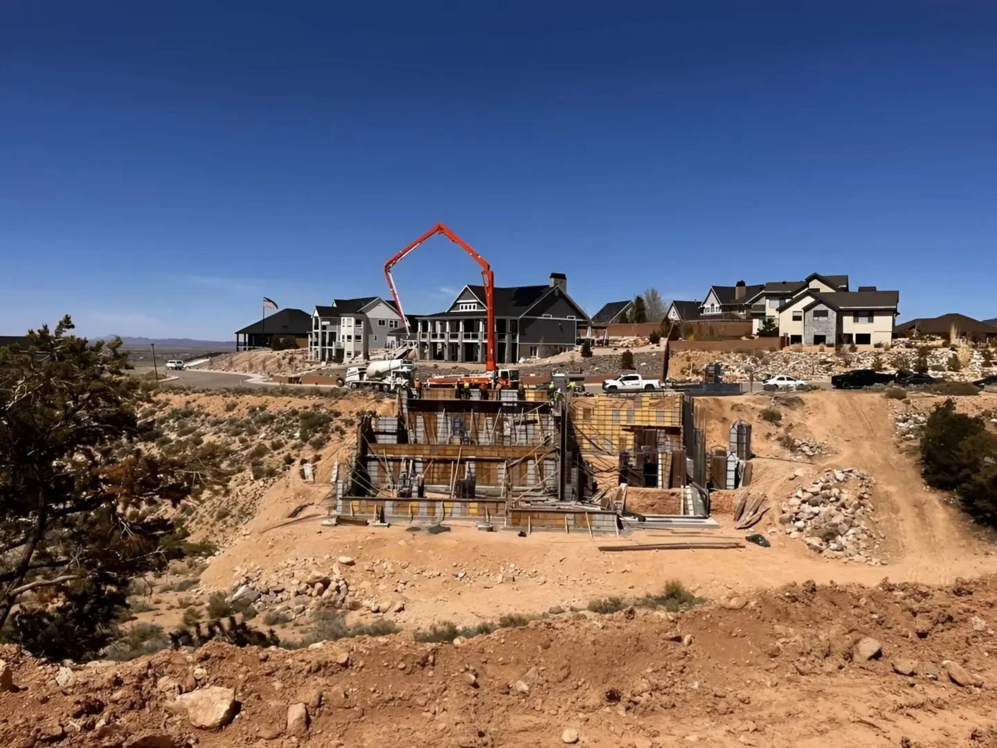 Housing construction site on a dirt hillside with excavated foundation and homes in the background