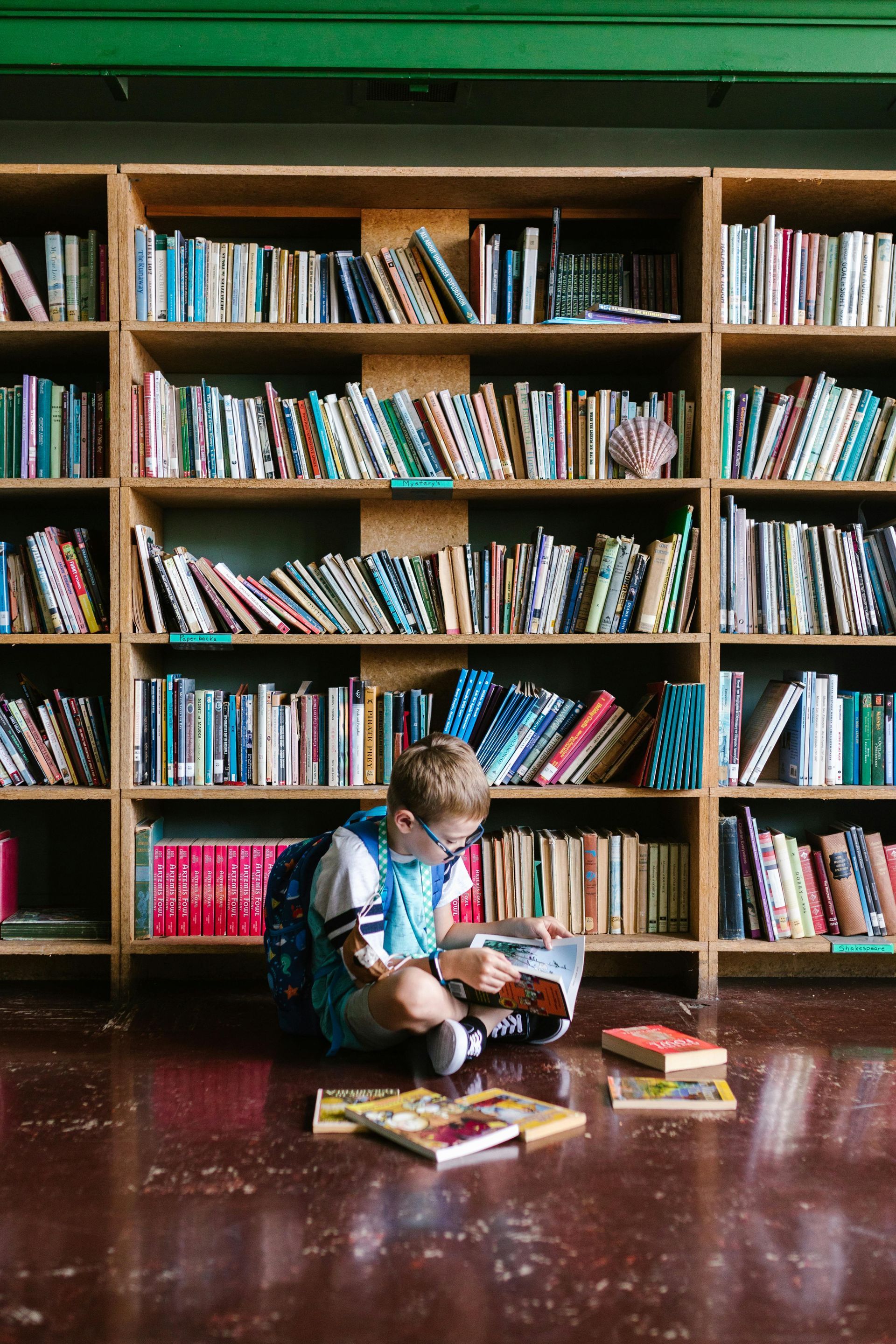 Montessori child is sitting on the floor reading a book in a library.