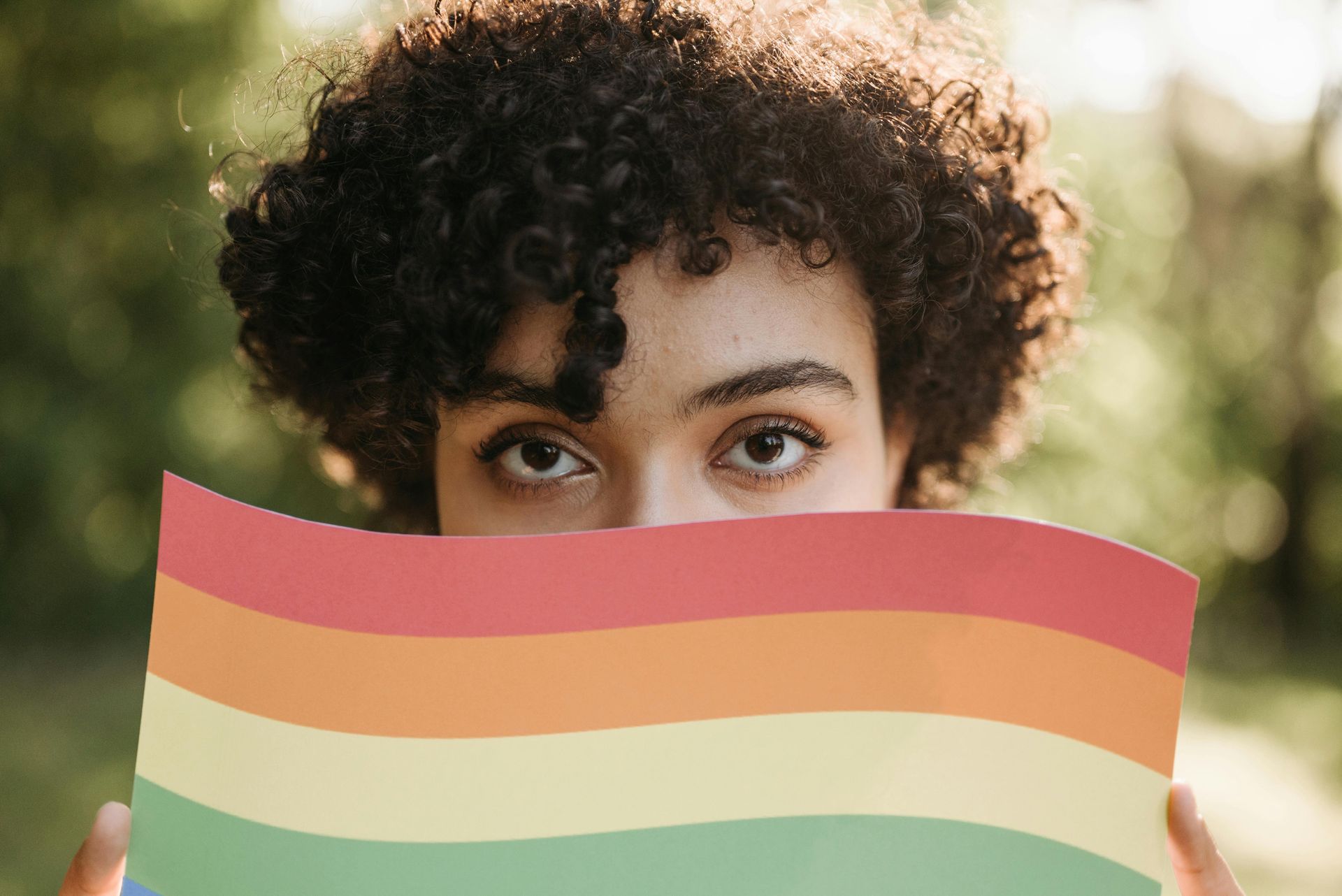 A woman is holding a rainbow flag in front of her face.