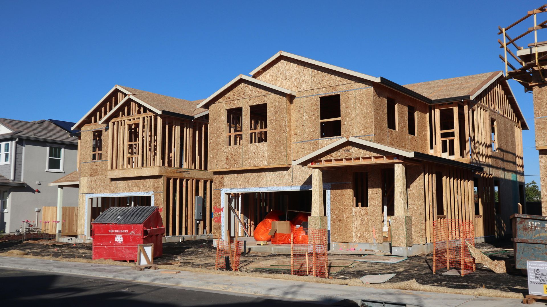 House under construction; wood framing visible, red dumpster, blue sky.