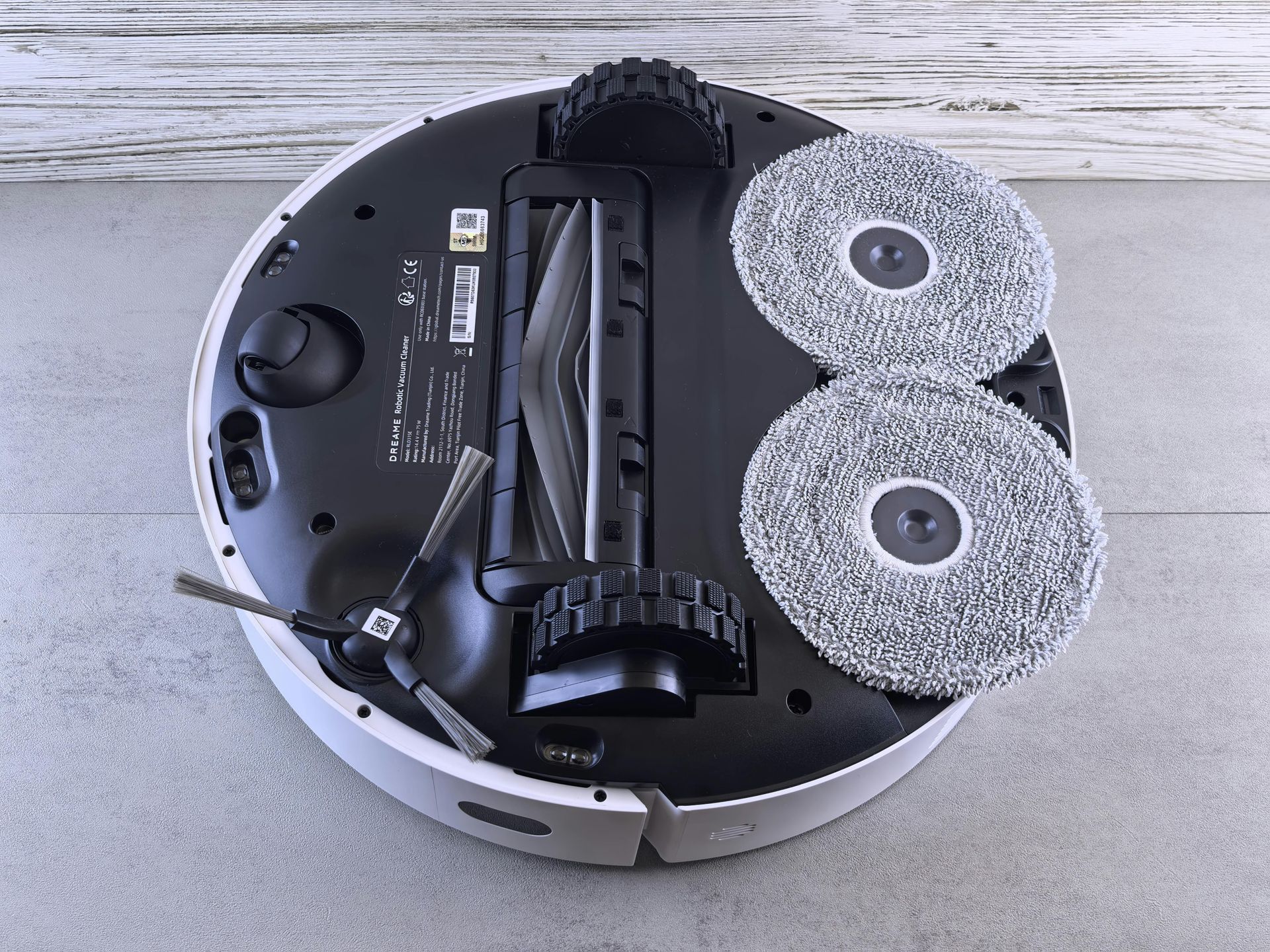 Bottom of a white robotic vacuum cleaner with two circular mop pads attached.