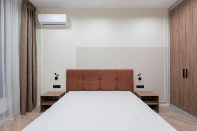 Bedroom with brown headboard, nightstands, and wardrobe. White walls, bed, and air conditioner.