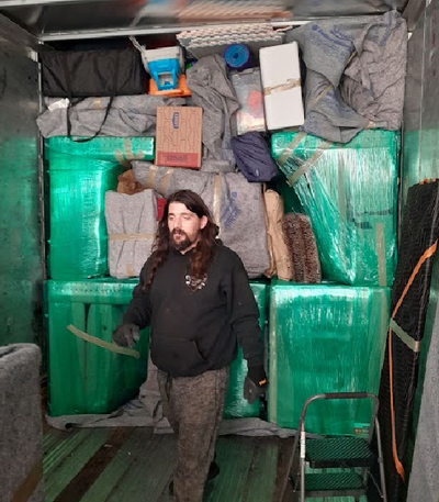 Man standing in a truck bed packed with wrapped cargo and boxes, holding a strap.