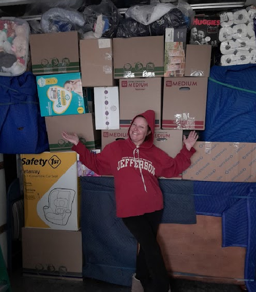 Person smiling in a red hoodie in front of stacked donation boxes and supplies.