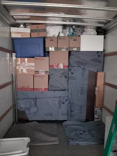 Packed moving truck with stacked cardboard boxes, bins, and wrapped furniture inside.