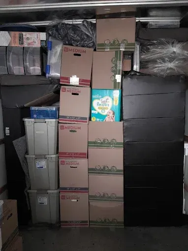 Stacked moving boxes and plastic storage bins in a cluttered storage room, with a detergent box visible.