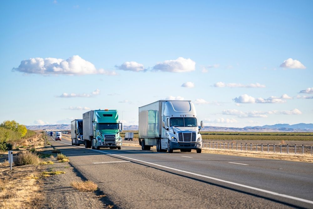 Two semi trucks driving on a rural highway under a bright blue sky