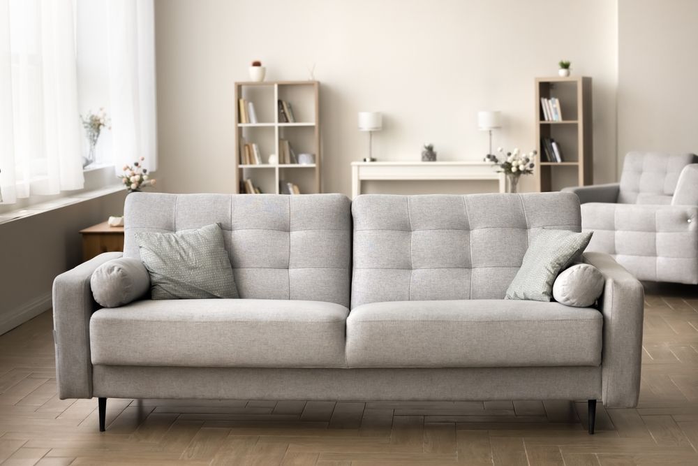 Bright living room with a gray sofa, cushions, shelves, and a fireplace on a wooden floor.