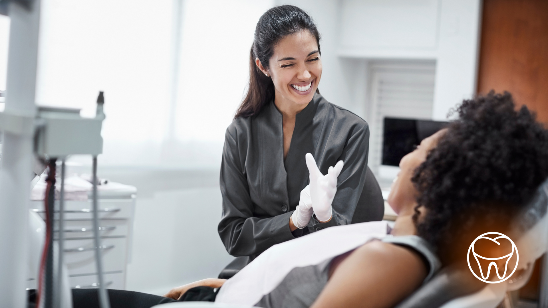 A female dentist is talking to a patient in a dental chair.