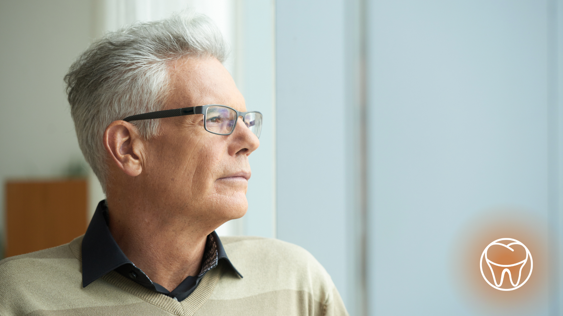 An older man wearing glasses is looking out of a window.