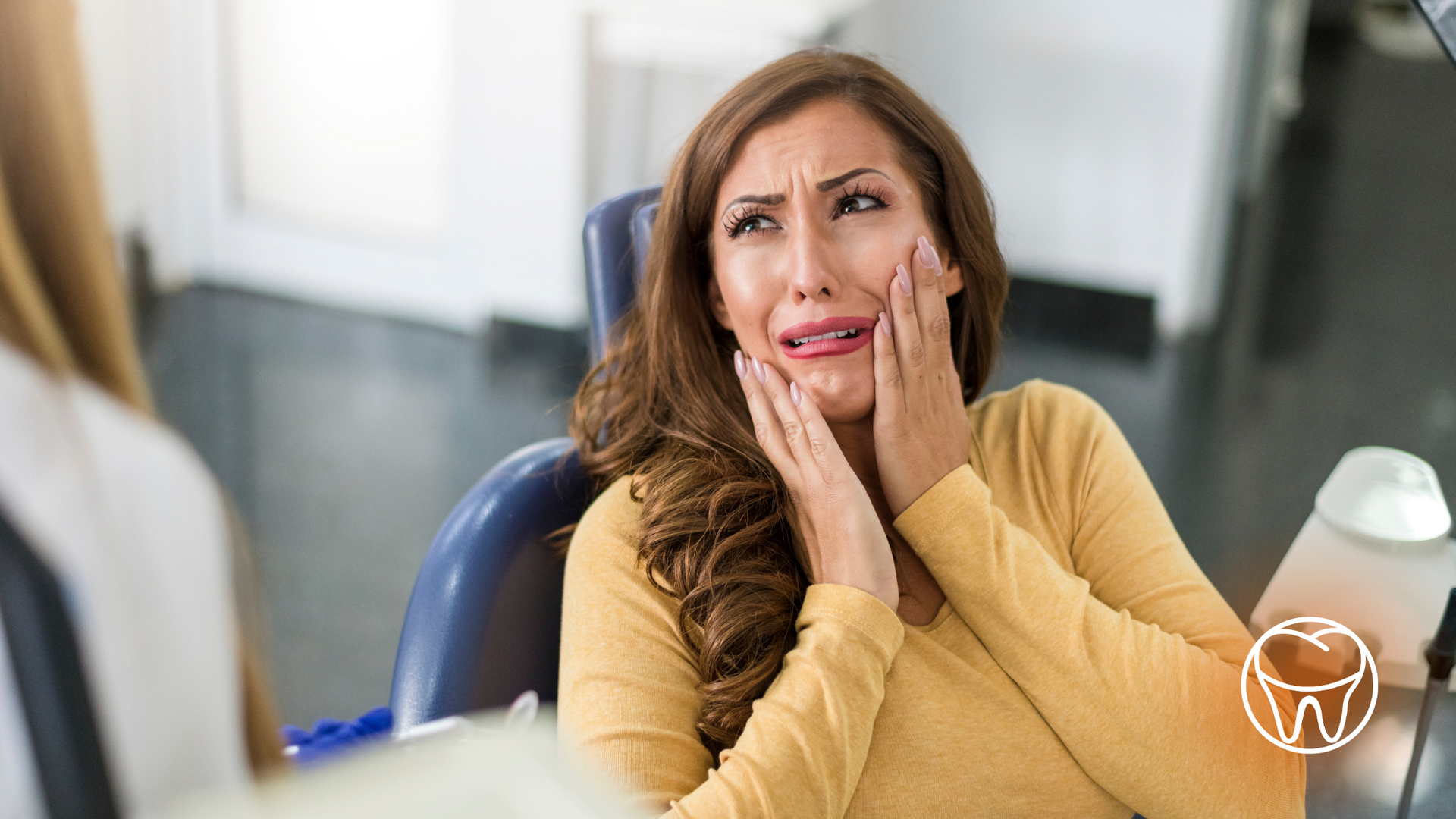 A woman is sitting in a dental chair with her hands on her face.