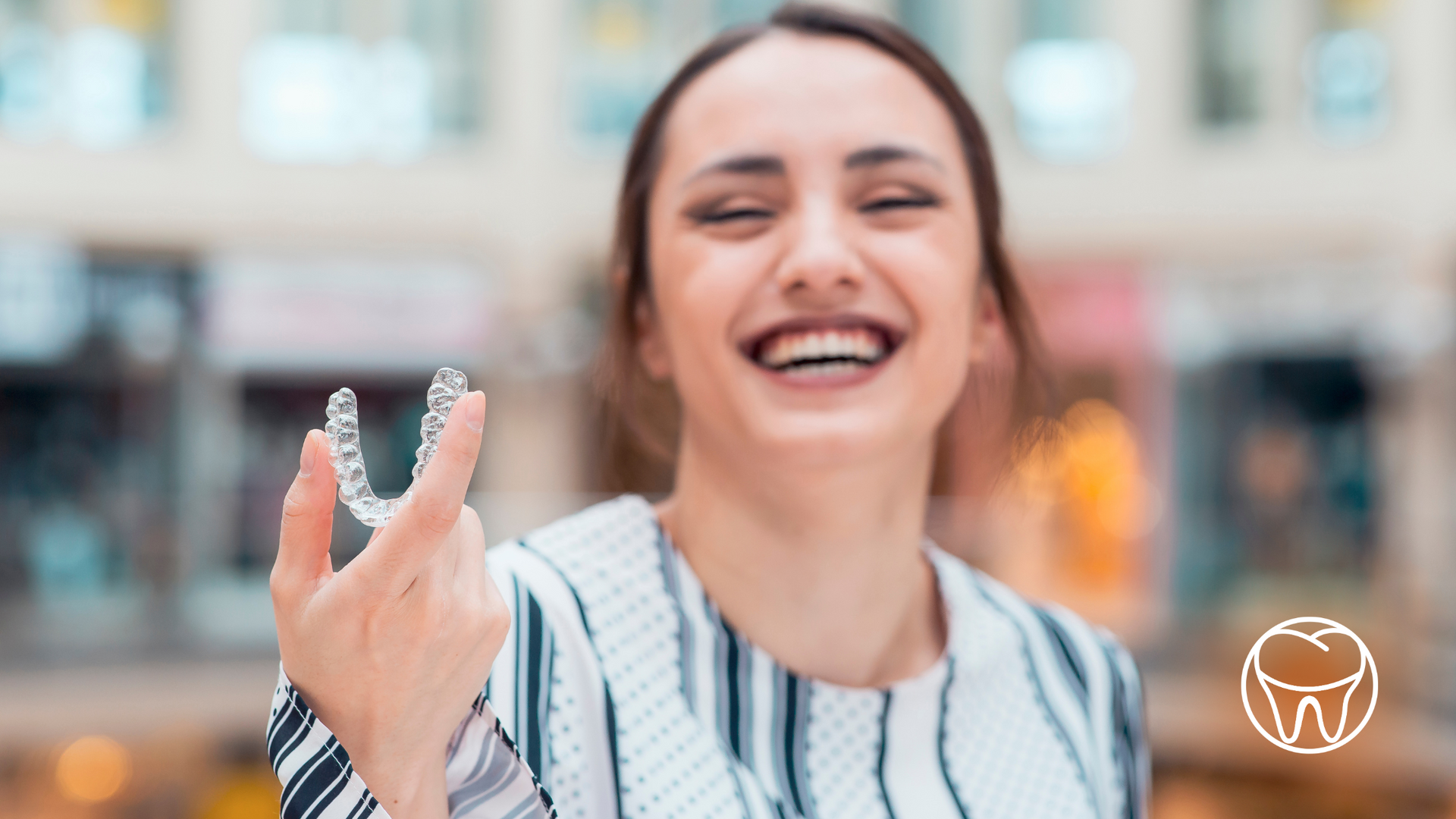 A woman is holding a clear retainer in her hand and smiling.