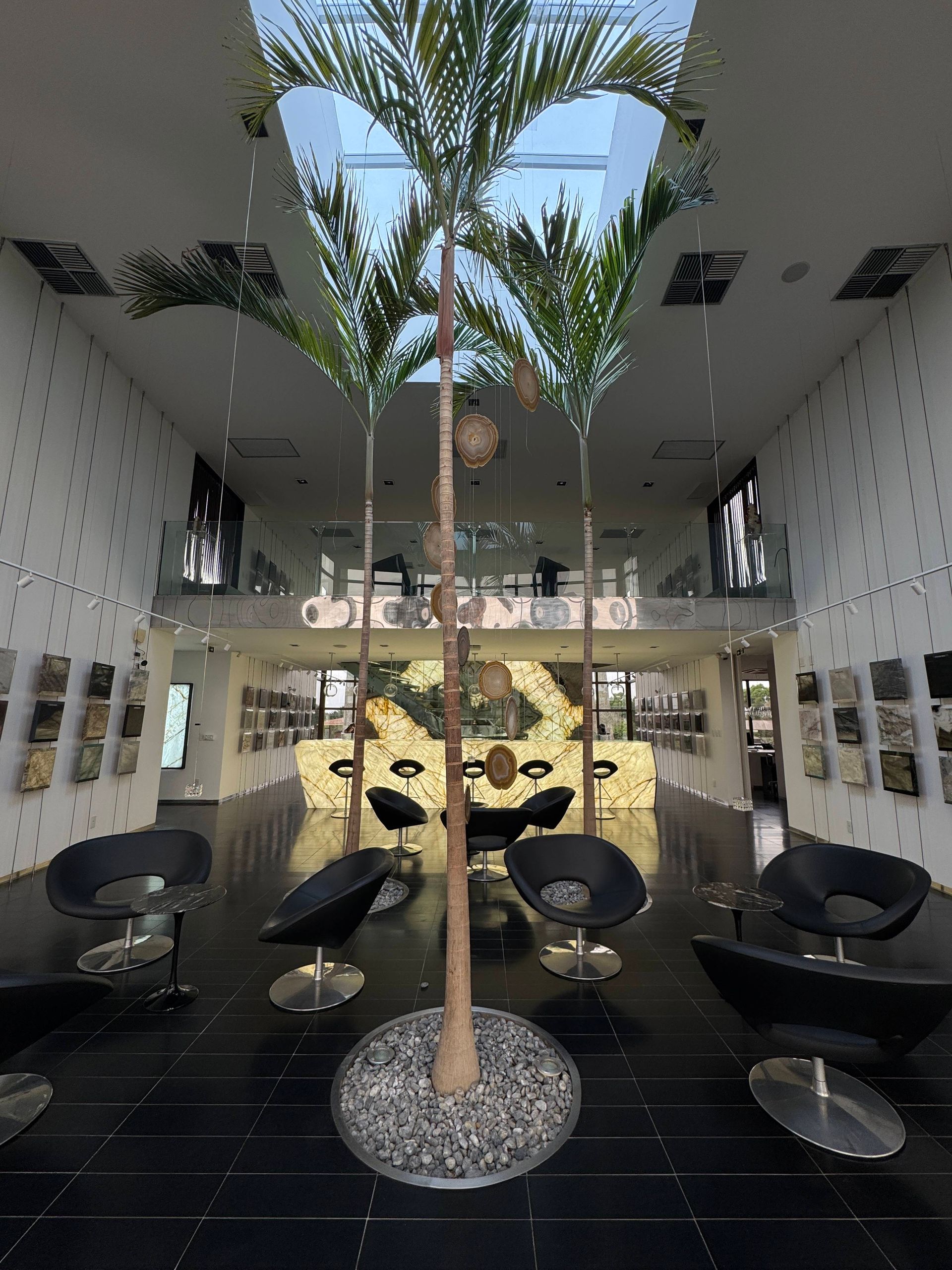 Modern lobby with tall palm trees, black lounge chairs, and a central decorative wall.