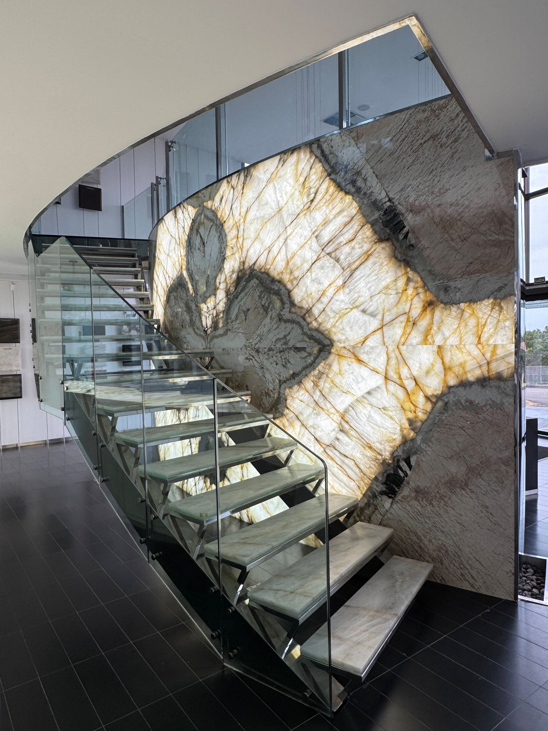 Modern staircase with glass railings and a large marble wall featuring a heart-shaped veined pattern