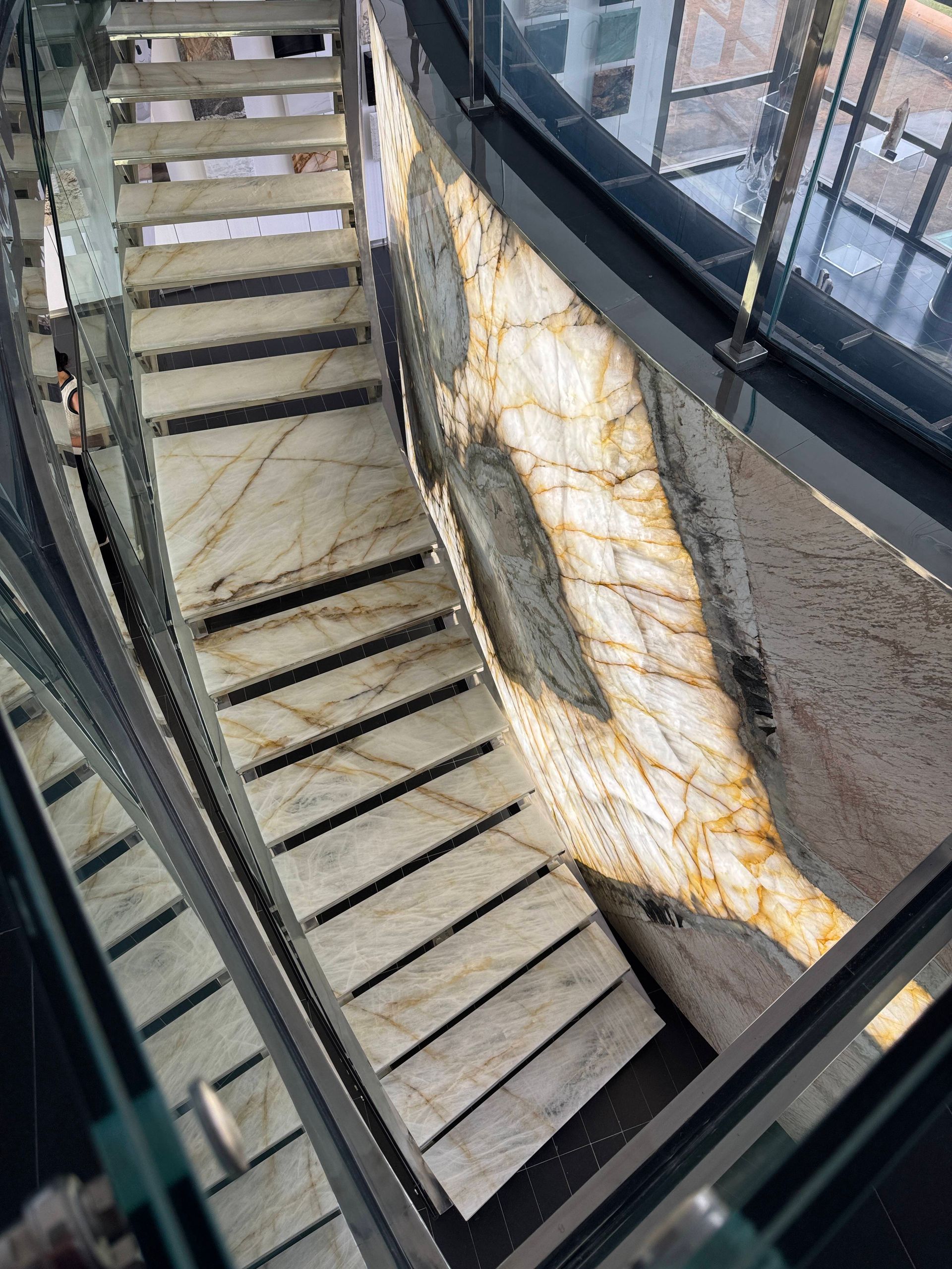 Curved stairwell with stone steps, glass railings, and a large patterned wall mural