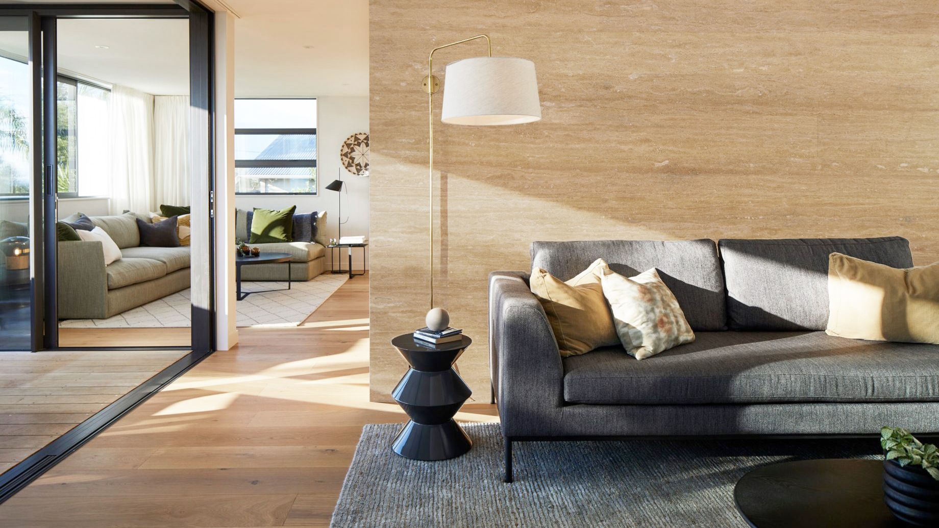 Modern living room with gray sofa, floor lamp, wood walls, and sliding glass doors opening to a bright terrace