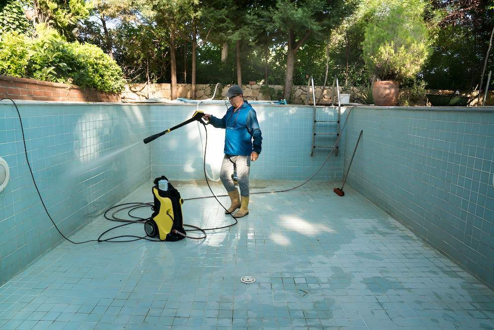 A Man is Cleaning a Swimming Pool With a High Pressure Washer — Sun City Pools In Hyde Park, QLD