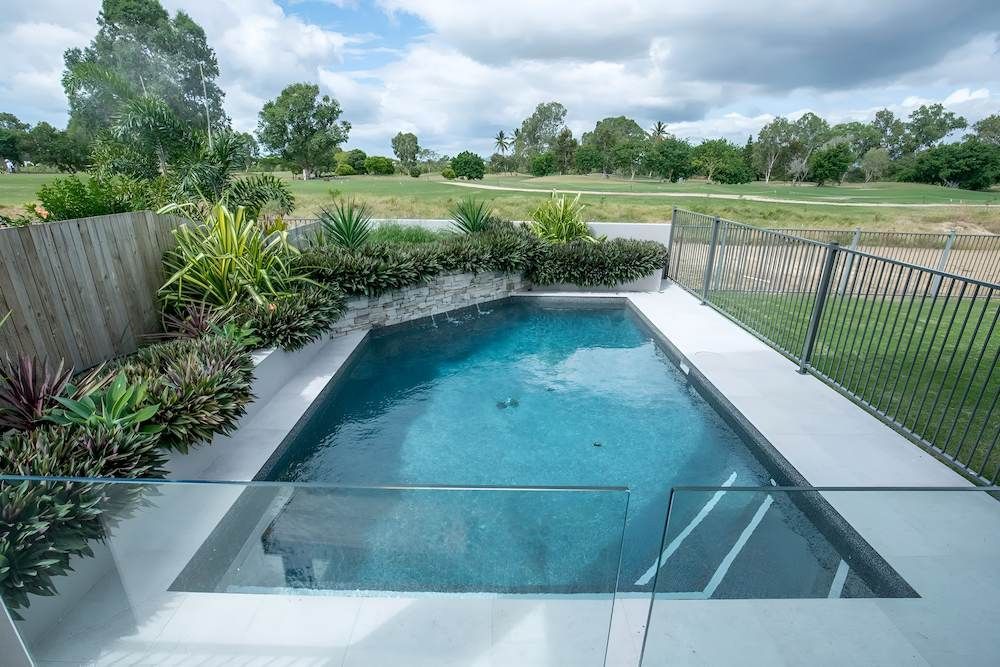 A Small Swimming Pool With a Glass Fence and a Golf Course in the Background — Sun City Pools In Hyde Park, QLD