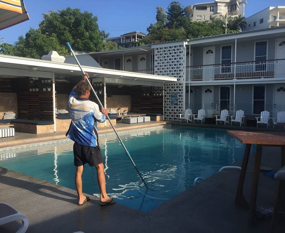 A Man is Cleaning a Swimming Pool With a Mop — Sun City Pools In Hyde Park, QLD