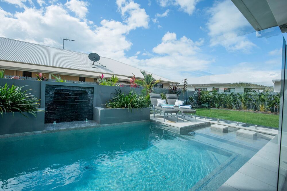 A Large Swimming Pool With a Waterfall in the Backyard — Sun City Pools In Hyde Park, QLD