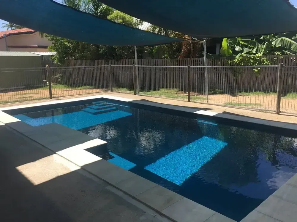 A Large Swimming Pool With a Blue Umbrella Over It — Sun City Pools In Hyde Park, QLD