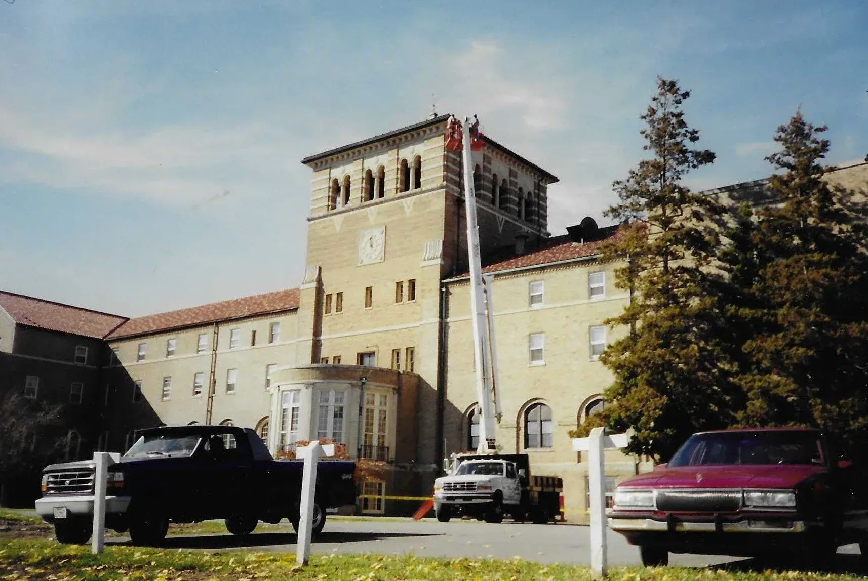 Historic beige building with tower and parked cars under a clear sky