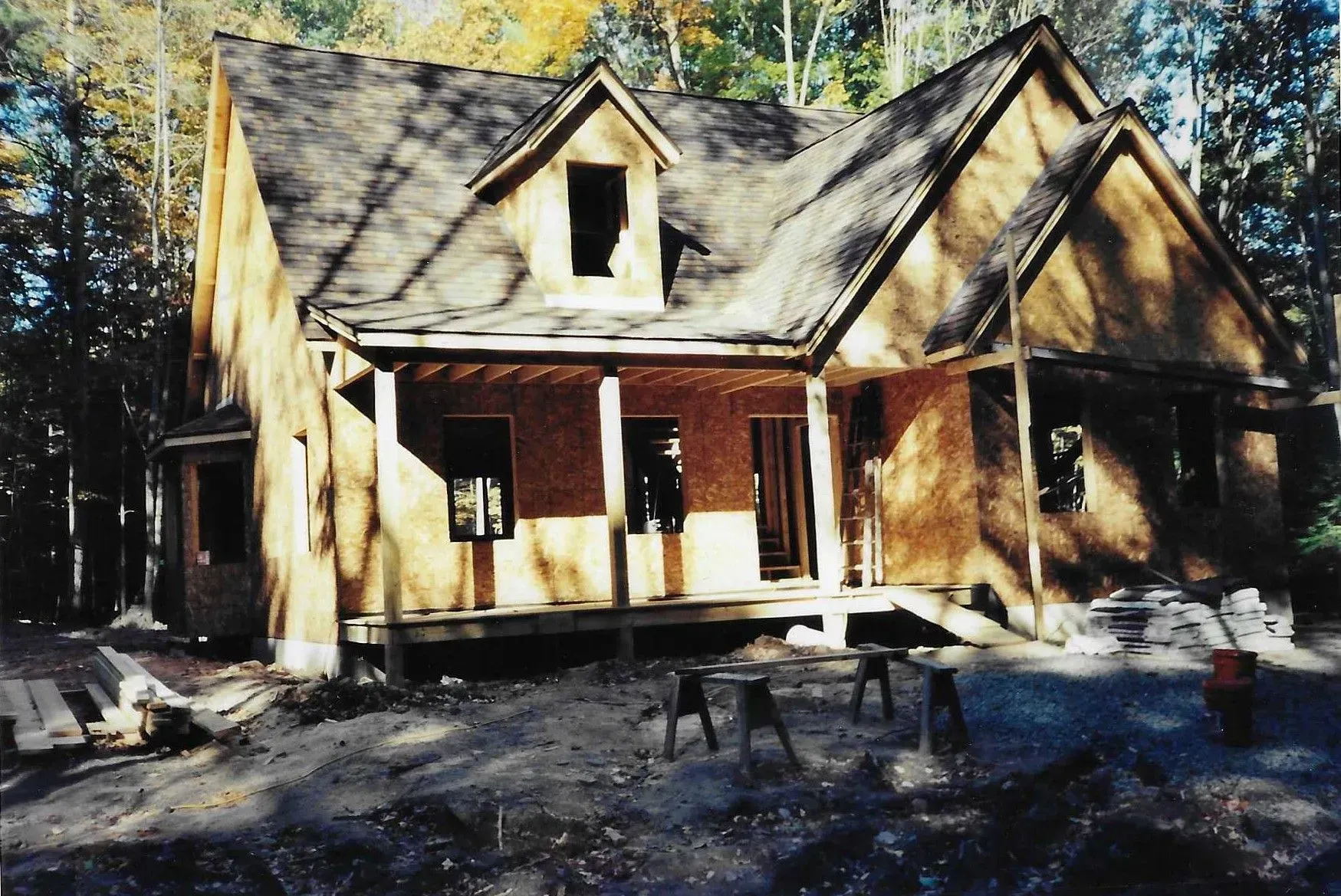 Brick house with steep roof and front porch in a wooded yard, lit by sunlight through trees