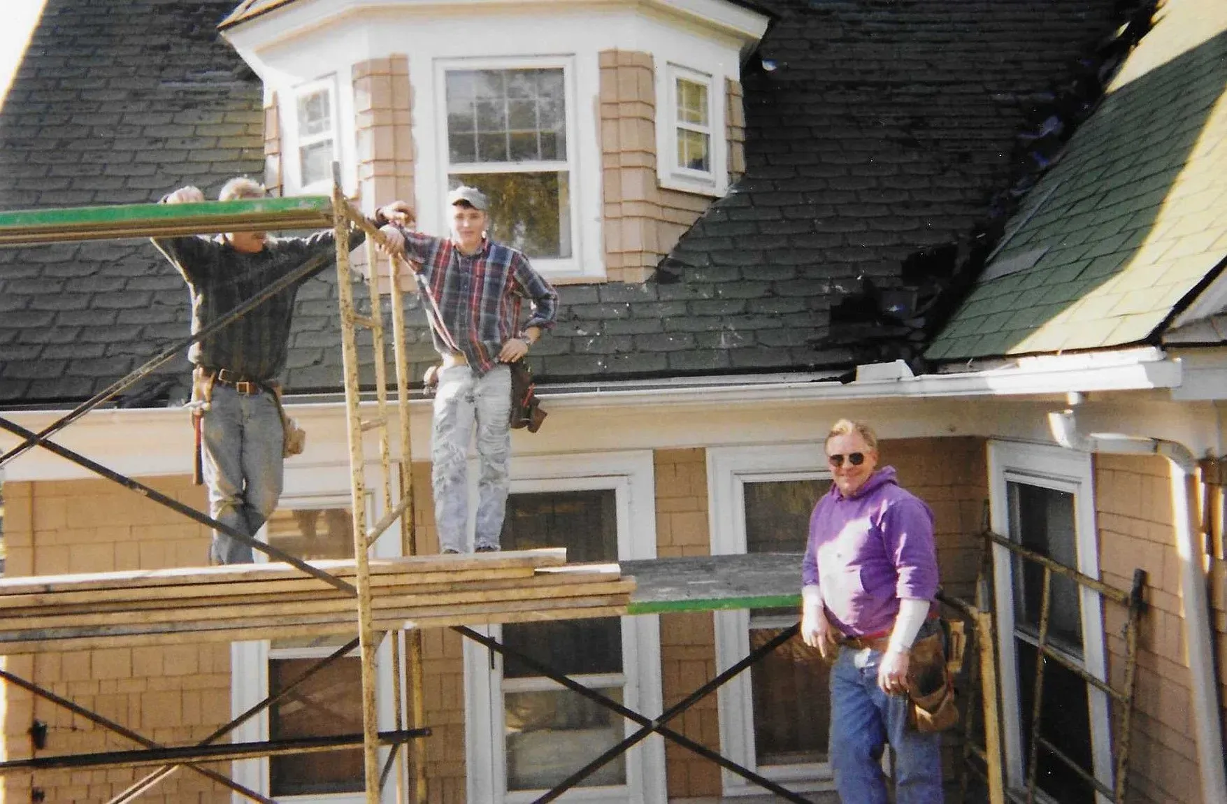 Workers on scaffolding repairing a house roof and exterior siding