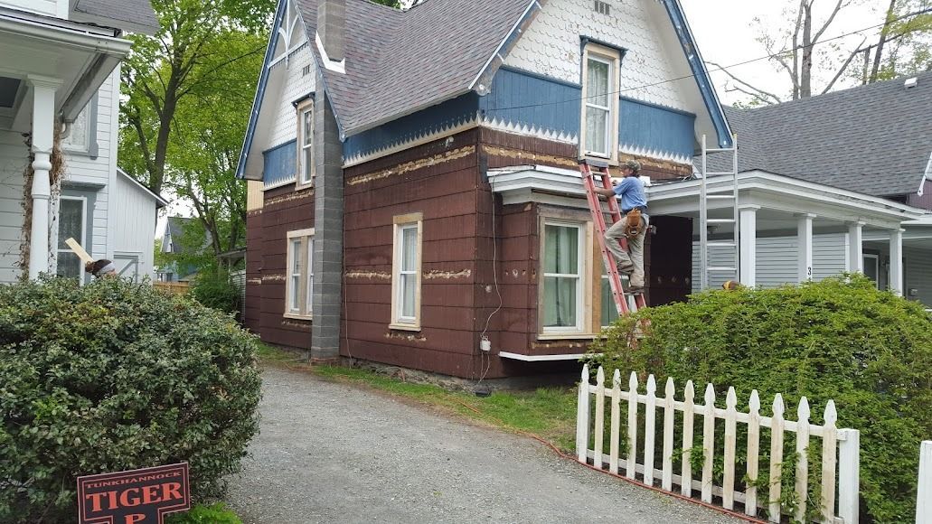 Small brick cottage with a blue roof, gravel path, and white picket fence in a garden setting