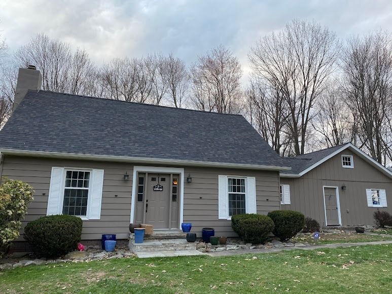 Single-story beige house with dark roof, white trim, blue planters, and a small front yard