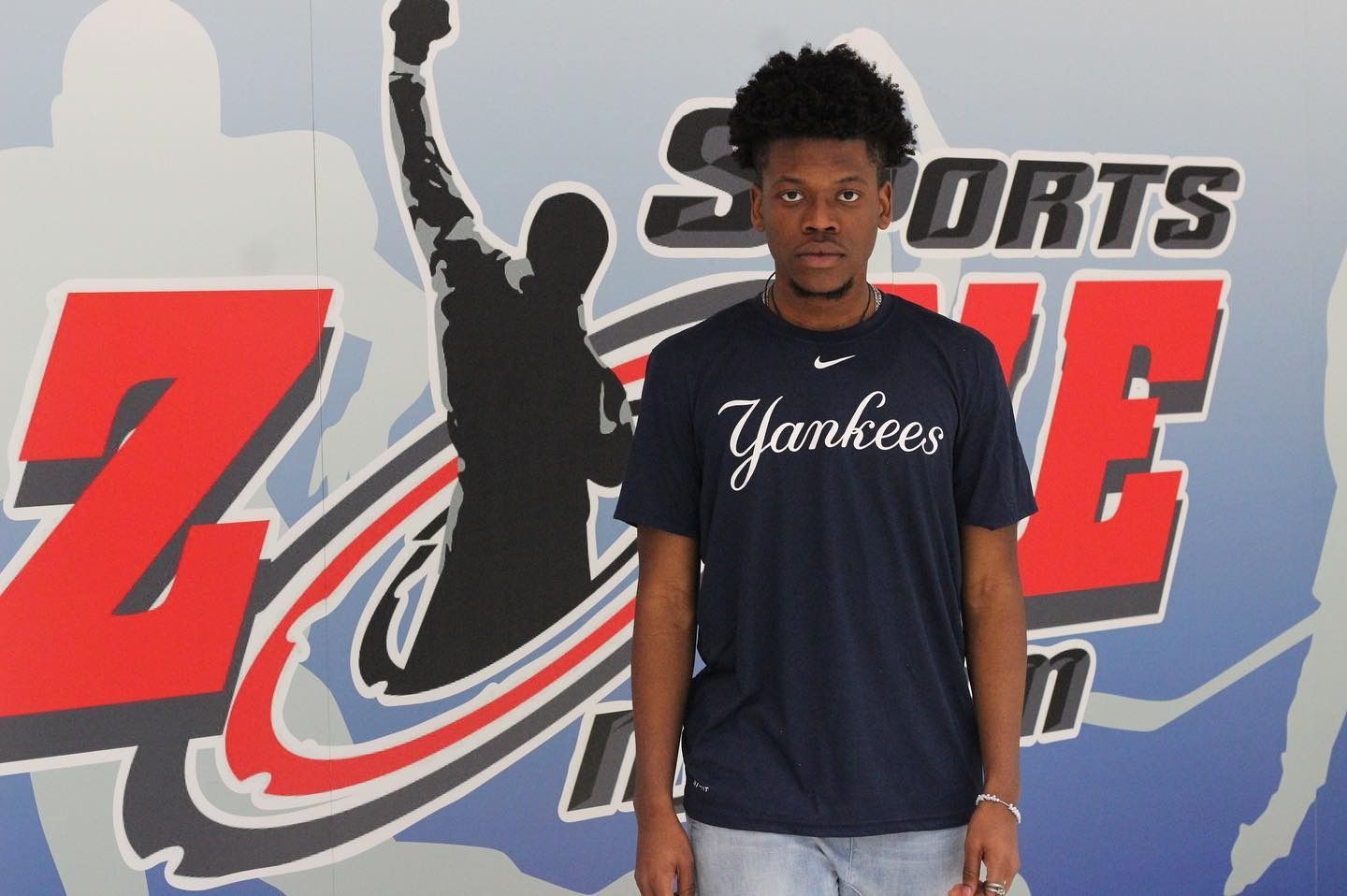Man wearing Yankees t-shirt stands in front of a sports-themed backdrop.