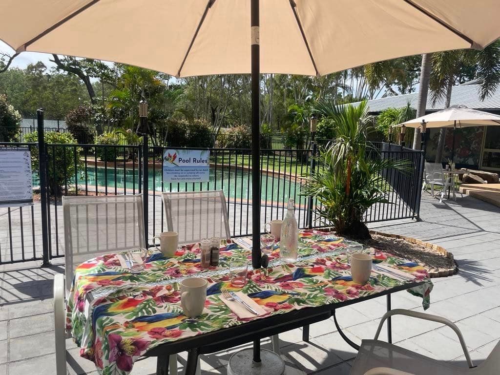 A Table And Chairs Under An Umbrella In Front Of A Pool — Heritage Resort in Nanum, QLD