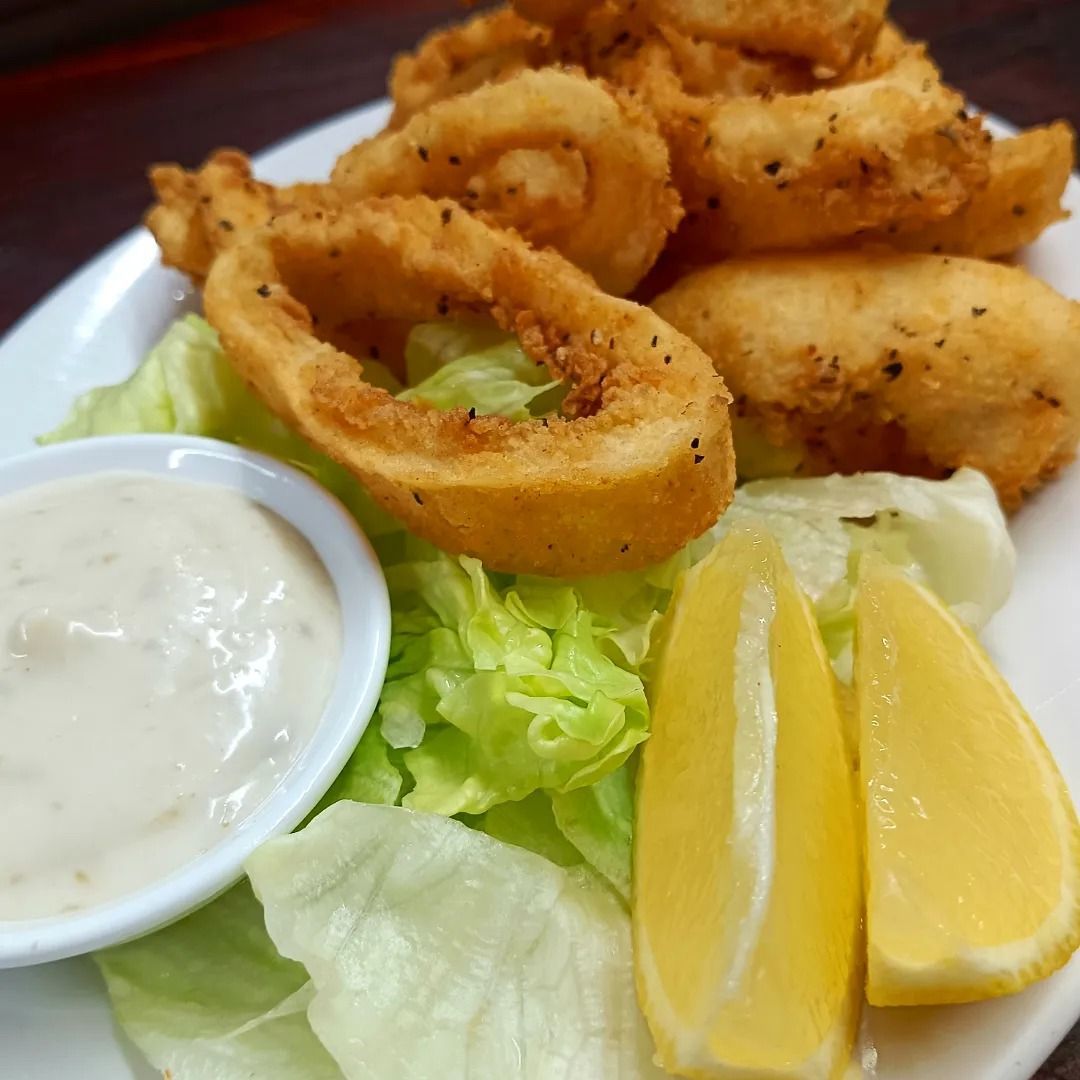 A White Plate Topped With Fried Calamari Rings, Lettuce, Lemon Slices And Ranch Dressing — Heritage Resort in Nanum, QLD