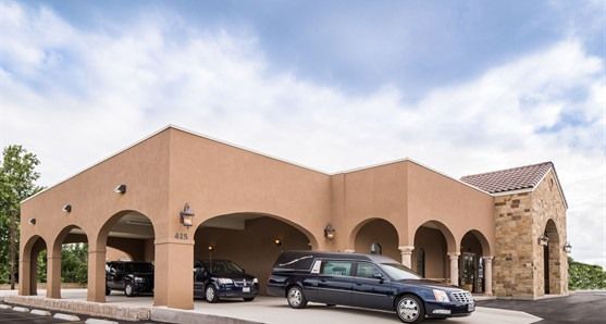 Tan stucco building with arches and parked cars under a partly cloudy sky