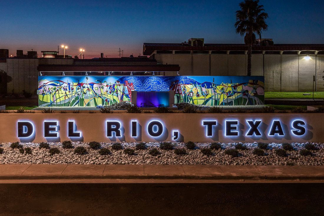 Illuminated “DEL RIO, TEXAS” sign with colorful mural at dusk