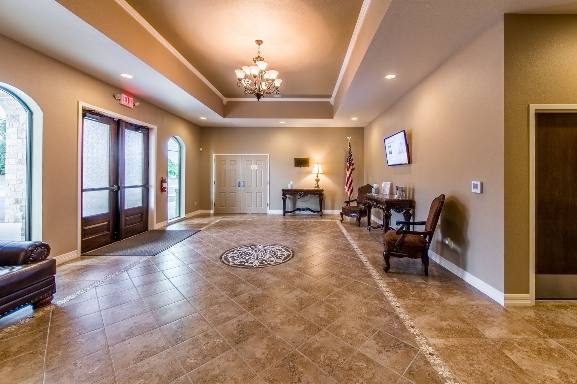 Spacious beige lobby with tiled floor, chandeliers, seating, and double glass doors.