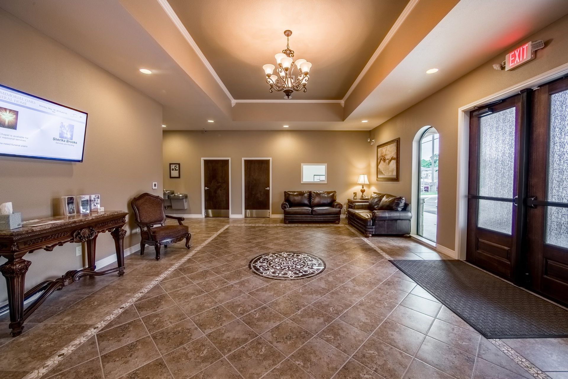 Spacious hotel lobby with chandelier, tiled floor, chairs, and glass entry doors