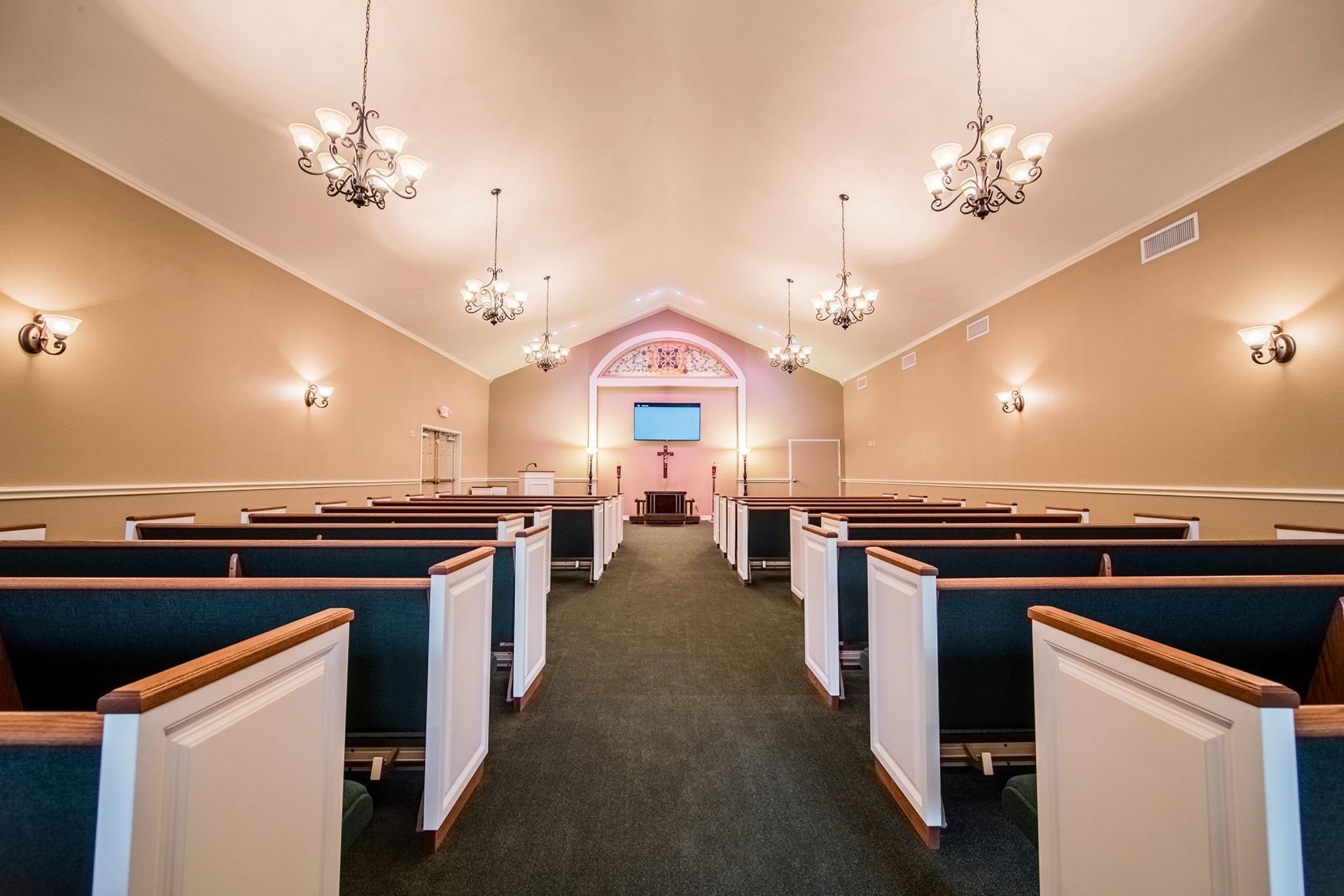 Empty church sanctuary with white pews, blue cushions, and chandeliers under a vaulted ceiling