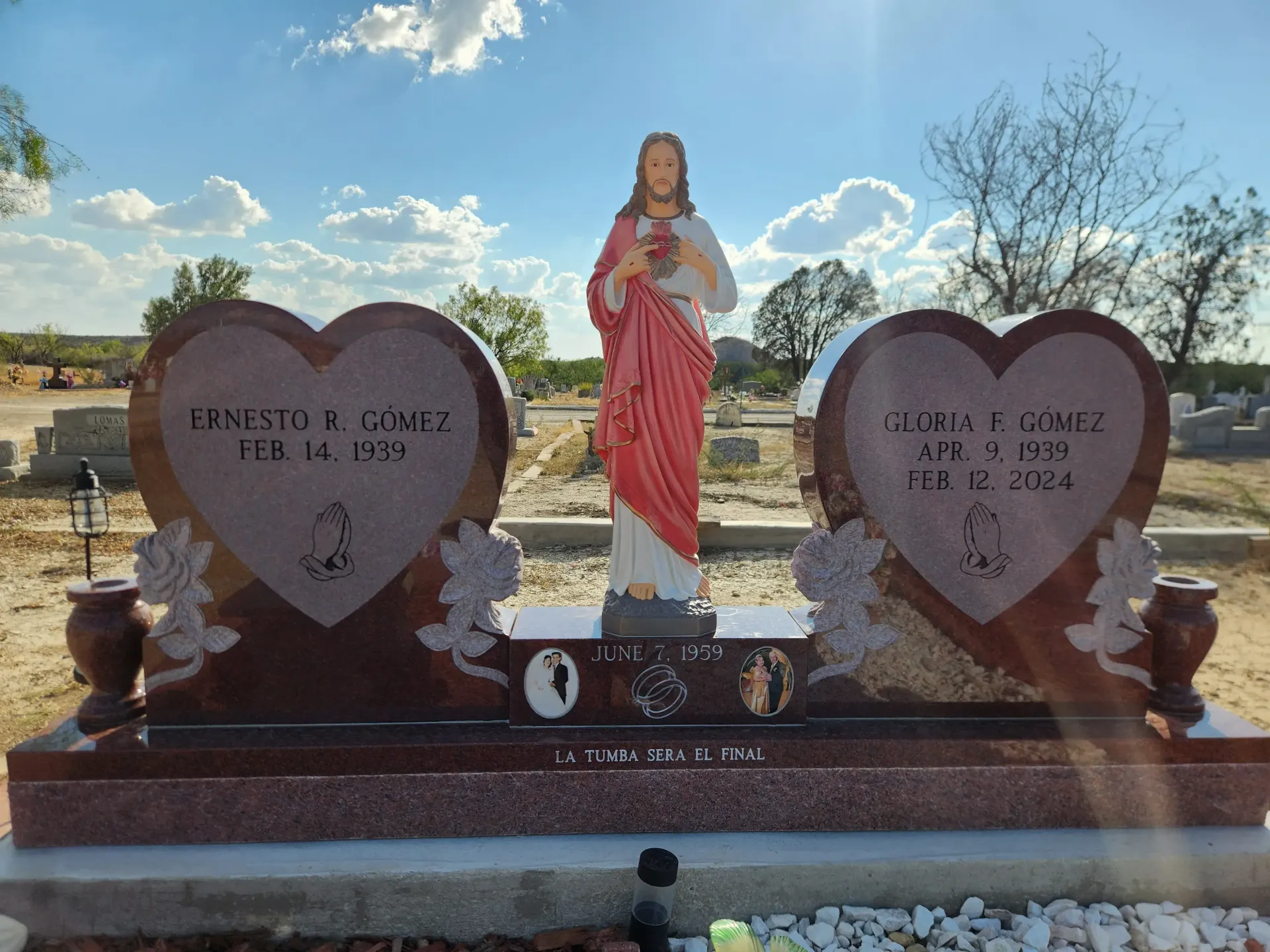 Gravestone with red-robed Jesus statue between two heart-shaped granite markers in a cemetery
