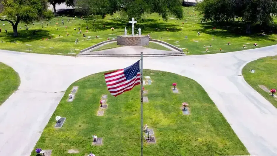 American flag flying over a small memorial with crosses in a grassy area and intersecting roads